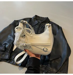 Detail of hobo bag with pearl chain, lace bow and decorative buckle on black leather background