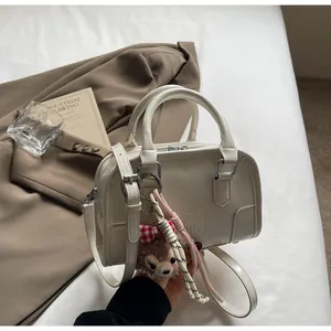 Detail view of cream Boston bag with embossed logo and LinaBell plush keychain accessory