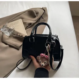 Detail of black embossed leather Boston bag with plush charm and detachable strap