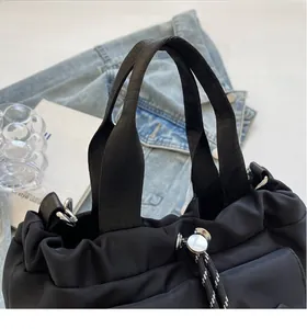 Detail of black nylon drawstring bucket bag with silver metal cord lock and webbing handles