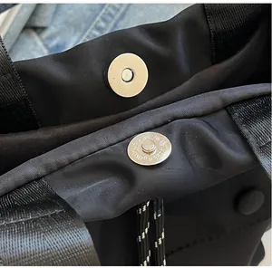 Detail of silver magnetic buckle and woven texture on a black nylon bucket bag