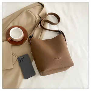 Detail of brown lychee grain leather bucket bag with embossed logo and shoulder strap