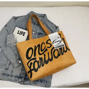 Flat lay of mustard yellow waterproof tote bag with black cursive text and denim jacket