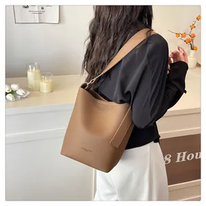 Close-up of brown pebbled leather bucket bag with wide strap on model's shoulder