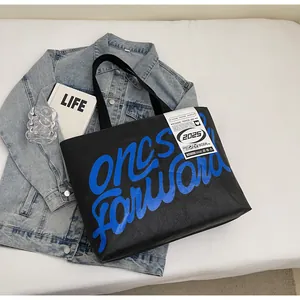 Close-up of black waterproof tote bag with blue graffiti text on white flat lay
