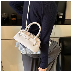 Close-up of a white leather shell-style Boston bag with decorative strap buckles and handles