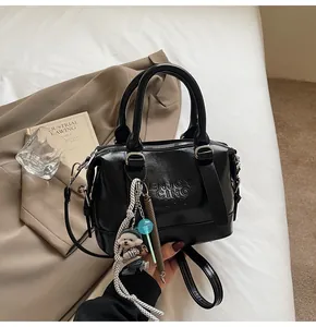 Detail of black glossy leather handbag with letter embossing and cute puppy charm