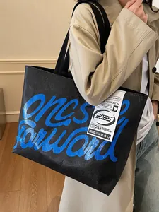 Fashionable black Tyvek tote bag with blue graffiti print worn by a model in lifestyle setting