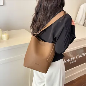 Brown lychee leather bucket bag with wide shoulder strap worn by a model in a cafe