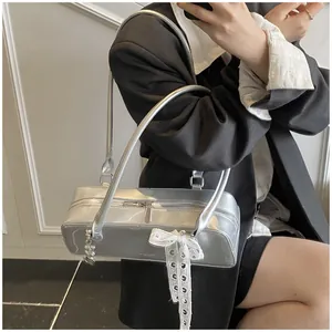 Détail d'un sac argenté brillant avec nœud en dentelle blanche et breloque en métal