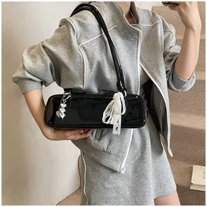 Détail du sac baguette en cuir verni noir avec cœurs argentés et nœud en dentelle