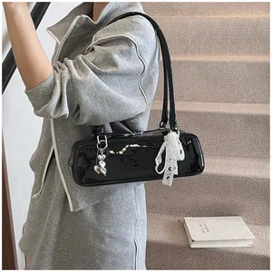 Détail du sac sous le bras en cuir verni noir avec charm cœur et ruban dentelle