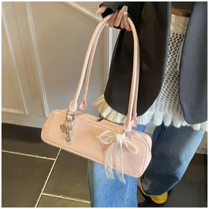 Détail du sac baguette en cuir verni rose avec breloque cœur argentée et nœud en dentelle
