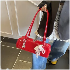 Gros plan du sac bandoulière en cuir verni rouge brillant avec breloque cœur et dentelle