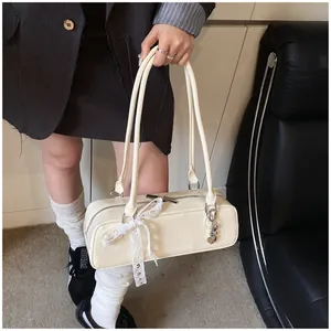 Détail du sac baguette en cuir crème avec nœud en dentelle et breloque ours argenté