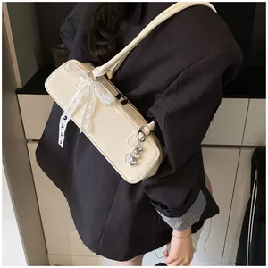 Détail d'un sac sous le bras blanc crème avec nœud en dentelle et breloque cœur en argent