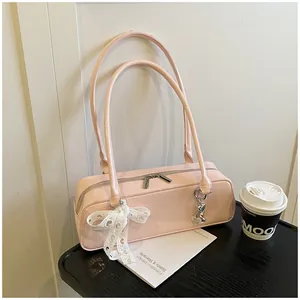 Détail du sac à bandoulière en cuir verni rose clair avec nœud en dentelle et breloque cœur