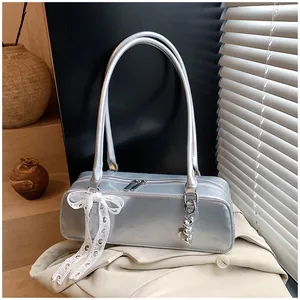 Détail du sac baguette argenté métallisé avec nœud en dentelle blanche et pendentif cœur
