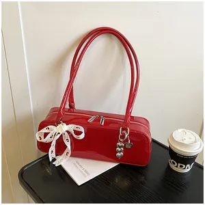 Détail du sac sous le bras en cuir verni rouge avec nœud en dentelle et pendentif cœur