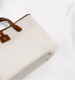 Detailed macro view of large white tote bag with brown leather handles and gold metal feet