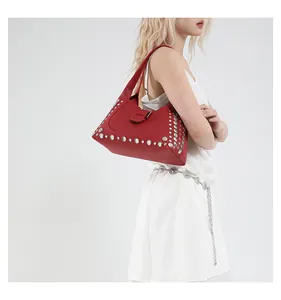 Dettaglio borsa hobo rossa con borchie argentate e fibbia su modella in abito bianco
