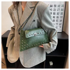 Détail du sac en cuir vert foncé avec clous argentés et bandoulière chaîne sur blazer gris