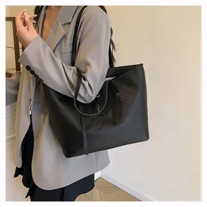 Close-up of black litchi grain leather tote bag worn by model in gray blazer