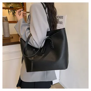 Detail of black pebbled leather tote bag with gold logo tag shown on a shoulder