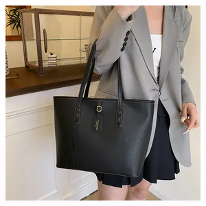 Macro detail of black lychee grain leather texture and gold hardware on large tote bag