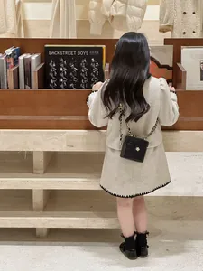 Détail d'une veste en tweed pour fille avec bordure zigzag noire et petit sac matelassé