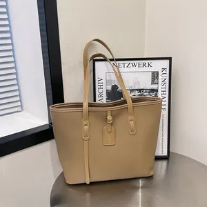 Minimalist large brown tote bag in pebbled leather with gold hardware on a metal stool