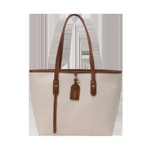 Minimalist large beige tote bag with brown leather handles and decorative brand tag