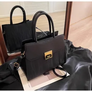 Detail of black textured leather handbag with gold metal lock shown via mirror reflection