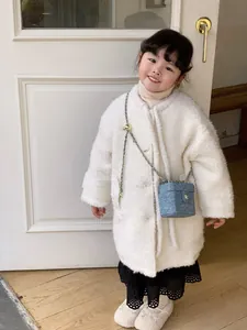 Détail d'un mini sac bleu matelassé avec chaîne dorée sur un manteau blanc en peluche