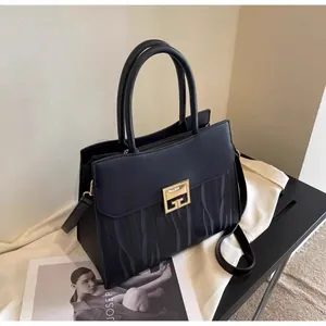 Close-up of black leather handbag featuring golden geometric lock and wavy textured pattern