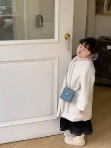 Détail d'un mini sac à chaîne en denim bleu porté avec un manteau en polaire blanche