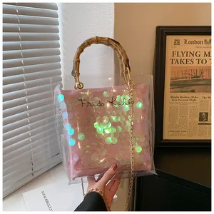 Detail of transparent PVC tote bag with pink sequins, bamboo handle, and gold chain strap