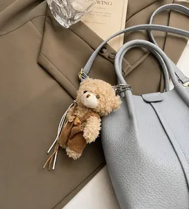 Close-up of a plush bear charm with corduroy overalls hanging on a light blue leather bag