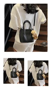 Detail of black lychee texture handbag featuring a cute bear plush charm and gold hardware