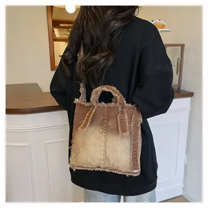 Brown gradient denim tote bag with frayed edges worn by a model in a cozy cafe setting