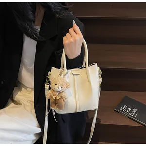 Detail of off-white lychee pattern bucket bag with a cute plush bear charm accessory