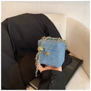 Détail du mini sac boîte en denim matelassé bleu clair avec fleur dorée et chaîne