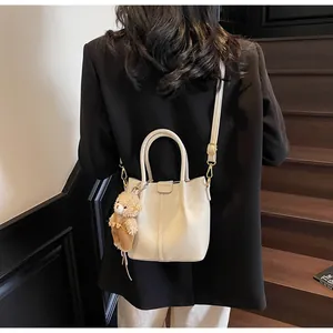 Detail of off-white lychee texture leather bucket bag with cute plush bear charm accessory