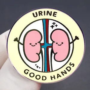 Cartoon kidney enamel pin with Urine Good Hands text on yellow circular metal badge