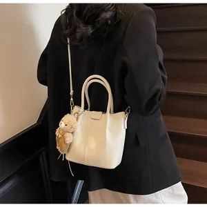 Detail of off-white lychee leather bucket bag with a cute plush bear charm decoration