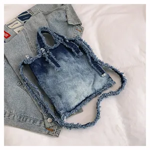 Close-up of washed denim tote bag showing frayed fringe edges and dual straps