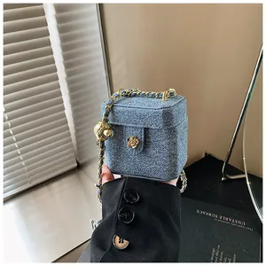Détail du mini sac boîte en denim bleu avec fermoir camélia doré et chaîne à boule dorée