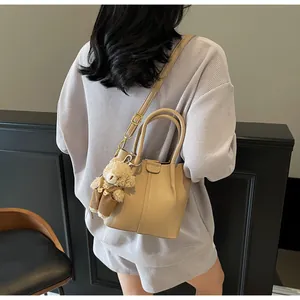 Close-up of beige lychee leather bucket bag with a cute plush bear pendant accessory