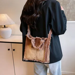 Brown distressed denim tote bag with frayed edges shown in a lifestyle shoulder view