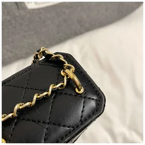 Détail du mini sac boîte en cuir noir matelassé avec chaîne dorée et œillets